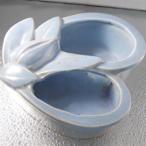 Könnte beinhalten: Ein hellblauer Keramik-Pflanztopf in Form einer Blume mit zwei separaten Pflanzbereichen.