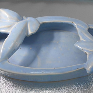 Pode incluir: Um prato de cerâmica azul claro com um design floral decorativo. O prato tem uma forma oval pouco profunda e uma borda elevada.