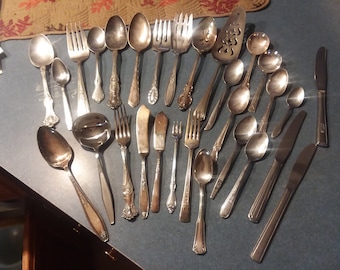 May include: A collection of vintage silverware, including spoons, forks, and a serving spoon. The silverware is made of silver and has a polished finish.