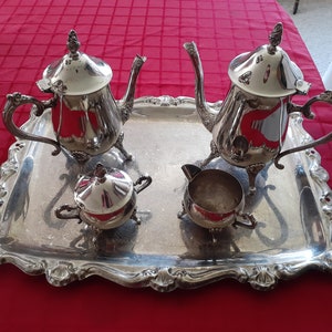May include: A silver tea set on a silver tray with an ornate design. The set includes a teapot, creamer, and sugar bowl.