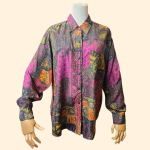 May include: A long-sleeved button-down shirt with a vibrant paisley pattern in shades of purple, black, green, orange, and yellow. The shirt features a classic collar, a chest pocket, and buttoned cuffs. The shirt is displayed on a mannequin.