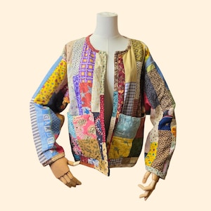 May include: A colorful patchwork jacket with a round neckline and two front pockets. The jacket features a variety of fabric patterns in shades of red, blue, yellow, and purple. The sleeve on the left side has the word "GARDEN" printed on it.