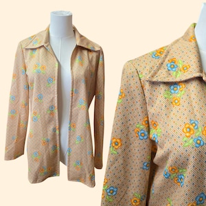 May include: Tan open-front jacket with a floral pattern in orange, blue, and green. The jacket has a collared neckline and long sleeves. The fabric has a subtle dotted texture.
