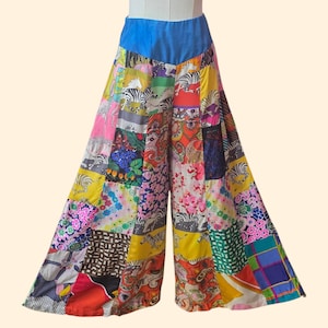 May include: Wide-leg patchwork pants with a blue waistband. The pants feature a vibrant mix of colorful fabric patches with various patterns, including floral, zebra stripes, and paisley designs. The pants are displayed on a mannequin.