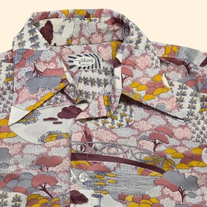 May include: A button-down shirt with a colorful landscape pattern. The shirt features a collar and a button closure. The pattern includes trees, bridges, and clouds in shades of pink, yellow, gray, and brown. The label reads "Viking".