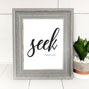 Puede incluir: Una impresión enmarcada con la palabra "seek" en elegante escritura negra. Debajo de la palabra está el texto "Psalm 119:2". El marco es gris con un acabado envejecido. Una pequeña planta en maceta con hojas verdes está a la derecha.