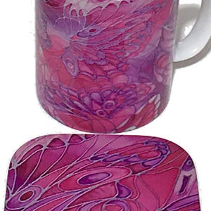 K&ouml;nnte beinhalten: Eine rosa und lila Keramiktasse mit einem Schmetterlingsdesign. Die Tasse wird mit einem passenden Untersetzer geliefert.