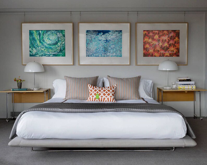 May include: A white bed with a gray bedspread and a white headboard. The bed is in a bedroom with three framed pictures on the wall above the headboard. The pictures are of abstract art in shades of blue, green, and orange.