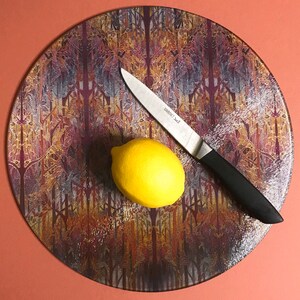 May include: A round, colourful chopping board with a lemon and a silver knife on top. The chopping board has a pattern of brown, orange, and purple.