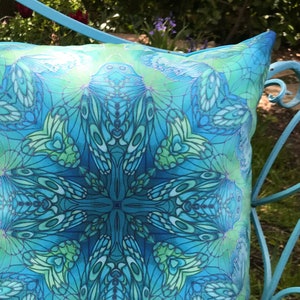 May include: A blue and green patterned pillow with a geometric design. The pillow is made of a soft, silky fabric and features a repeating pattern of butterfly wings.