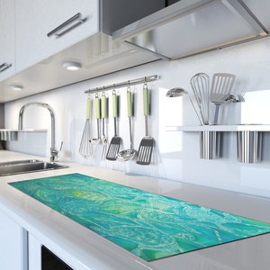 May include: A turquoise and green abstract kitchen runner with a white background. The runner is placed on a white countertop in a modern kitchen.