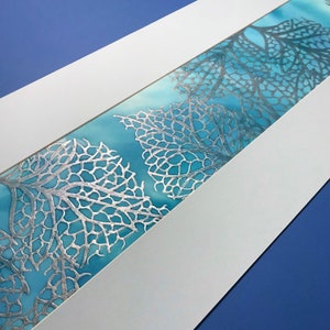 May include: A white mount with a blue and silver leaf design. The design is a repeating pattern of leaves with a delicate, intricate pattern.