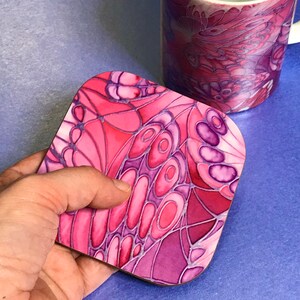 K&ouml;nnte beinhalten: Untersetzer mit einem Schmetterlingsdesign in Pink und Lila. Der Untersetzer ist aus einem harten Material gefertigt und hat eine gl&auml;nzende Oberfl&auml;che.