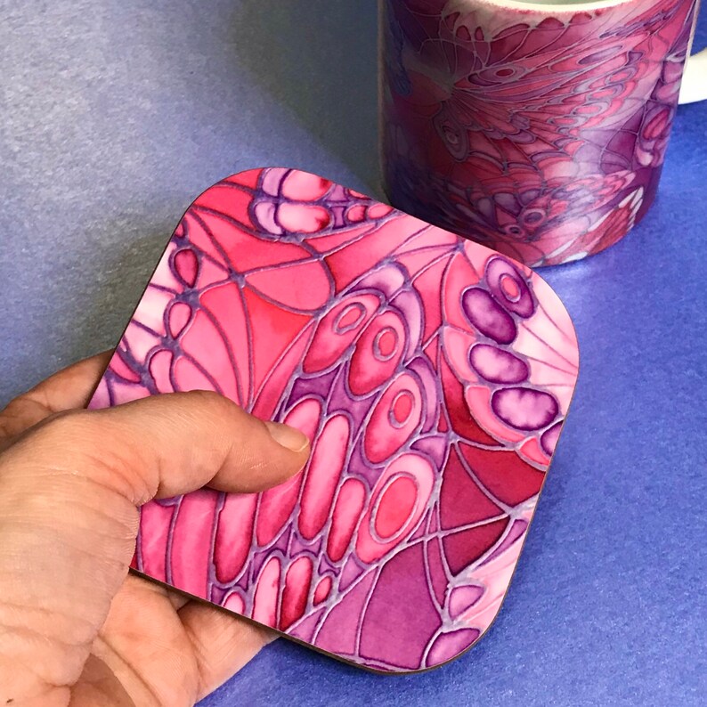 K&ouml;nnte beinhalten: Untersetzer mit einem Schmetterlingsdesign in Pink und Lila. Der Untersetzer ist aus einem harten Material gefertigt und hat eine gl&auml;nzende Oberfl&auml;che.