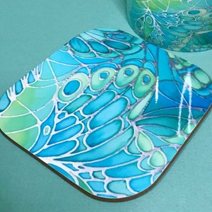 May include: A square blue and green coaster with a geometric pattern. The coaster has a glossy finish and is made of cork.