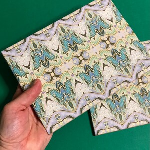 May include: Two decorative paper covered notebooks with a blue, green and gold geometric pattern. The notebooks are stacked on top of each other.