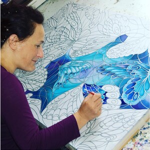 May include: A person paints a blue and white abstract painting with a brush. The painting features a design of overlapping butterfly wings.