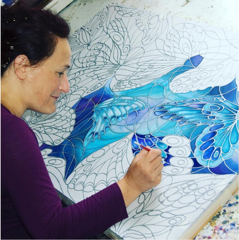 May include: A person paints a blue and white abstract painting with a brush. The painting features a design of overlapping butterfly wings.