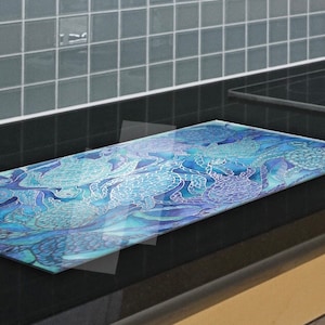May include: A blue and purple glass stovetop protector with a patterned design of sea creatures. The protector is on a black countertop.