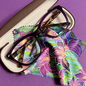 May include: Purple eyeglasses with tortoiseshell frames in a brown case with a floral patterned cleaning cloth.
