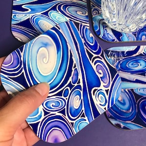 May include: Set of four blue and purple swirl patterned coasters. The coasters are made of a hard material and have a glossy finish.