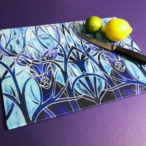 May include: A blue and white glass chopping board with a stylised deer design. The board is on a purple surface with a knife and two lemons.
