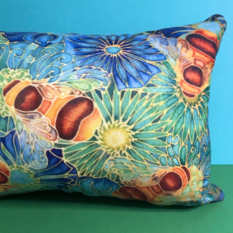 May include: A decorative pillow with a blue, green, and yellow floral pattern and a stylized bee design.