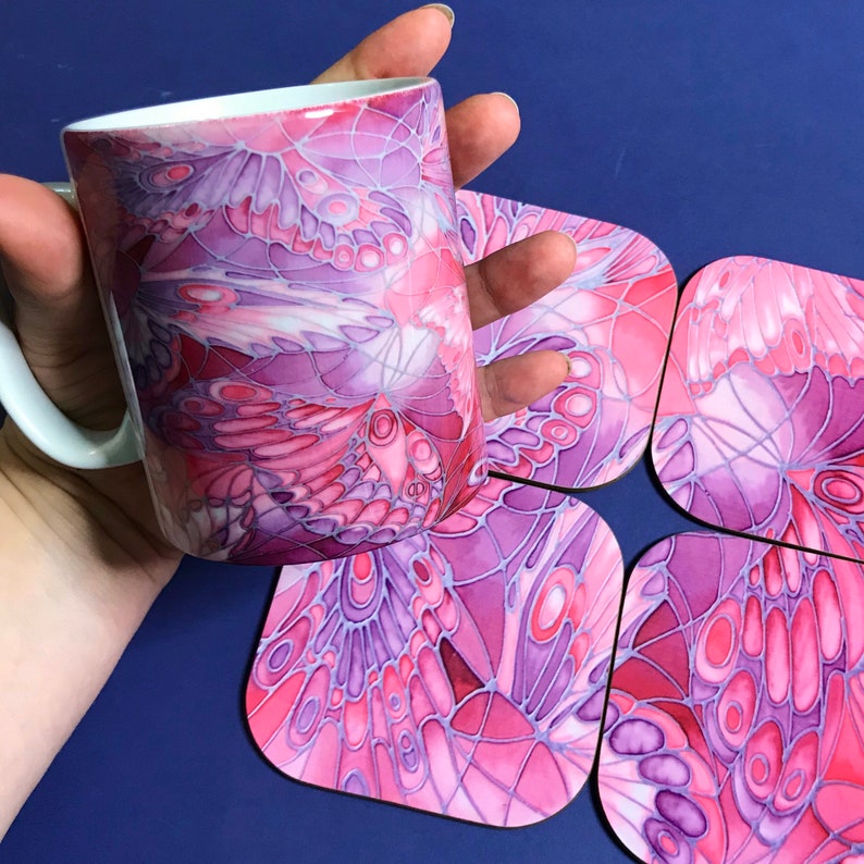 K&ouml;nnte beinhalten: Ein Set aus vier Untersetzern in Rosa und Lila mit einem Schmetterlingsfl&uuml;gel-Design. Die Untersetzer sind aus Keramik und haben eine gl&auml;nzende Oberfl&auml;che. Eine Tasse mit dem gleichen Design ist ebenfalls abgebildet.