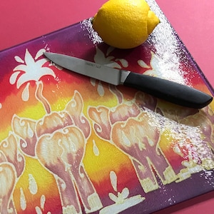 May include: A yellow lemon and a stainless steel paring knife with a black handle sit on a decorative cutting board. The board has a colourful design with orange, yellow, and purple hues.