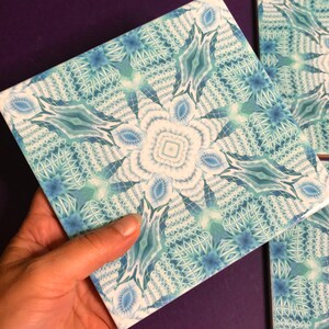 May include: A square ceramic tile featuring a blue and white geometric pattern. The design is intricate and includes a central flower-like motif.