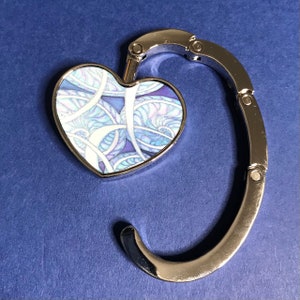 May include: A silver heart-shaped purse hook with a blue and white patterned design.