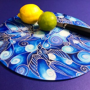 May include: A round cutting board with a blue and white patterned design. A lime and a lemon are on top of the board, with a black knife lying beside them.