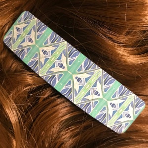 May include: A rectangular hair clip with a geometric pattern in shades of blue, green, and white.
