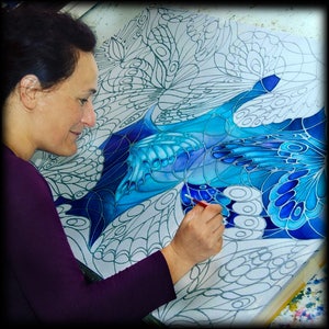 May include: A person paints a blue and white abstract design on a canvas with a fine-tipped brush. The design features intricate patterns and swirls, resembling butterfly wings.