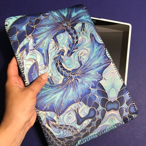 May include: A blue and white tablet case featuring a dragon design. The case has a zip closure and a soft, velvety lining.