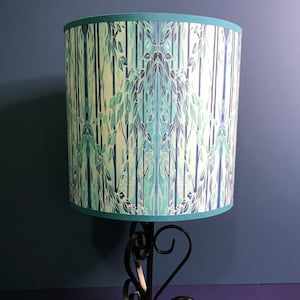 May include: A teal blue lampshade with a forest pattern on a black metal lamp base.