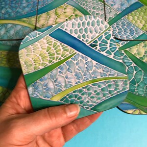 May include: A set of four coasters featuring a mosaic pattern in shades of green, blue and white. The coasters are made from a durable material and are ideal for protecting your furniture from scratches and spills.