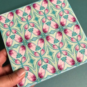 May include: A repeating pattern of pink and green floral shapes on a white background. The design is symmetrical and creates a sense of movement.