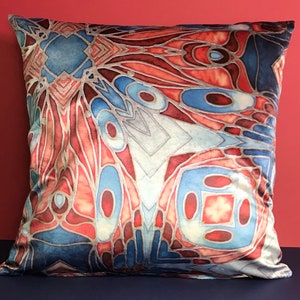 May include: A decorative throw pillow with a geometric pattern in shades of blue, red, and white. The pillow has a soft, velvety texture.