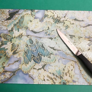 May include: A glass chopping board with a blue, white and gold butterfly design. A silver knife with a black handle is on the board.