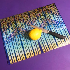 May include: A glass chopping board with a blue and gold forest design. A lemon and a silver knife are on the board.