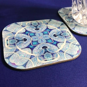 Könnte beinhalten: Ein quadratischer Untersetzer mit einem blauen, weißen und violetten Mandala-Design. Der Untersetzer ist aus Kork und hat eine glatte, glänzende Oberfläche.