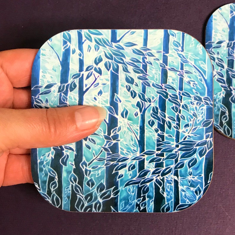 May include: A square blue and white coaster with a design of trees and leaves. The coaster has a rounded edge and is made of a durable material.