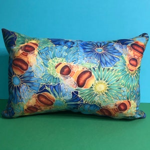 May include: A decorative pillow with a colorful floral pattern featuring bees and blue, green, and yellow flowers. The pillow is made of a soft, plush fabric.