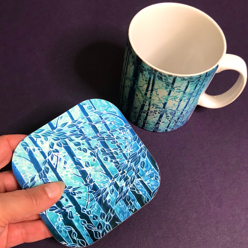 May include: A blue and white ceramic mug with a forest scene design. The mug is paired with a matching square coaster.