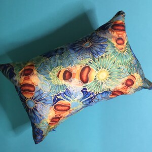 May include: A decorative pillow with a blue, green, and yellow floral pattern featuring stylized bees. The pillow is made of a soft, textured fabric.