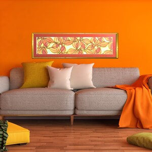 May include: A framed artwork with a colorful abstract design of leaves in shades of orange, red, and yellow. The artwork is hanging on a bright orange wall above a gray couch with pillows and a throw blanket.