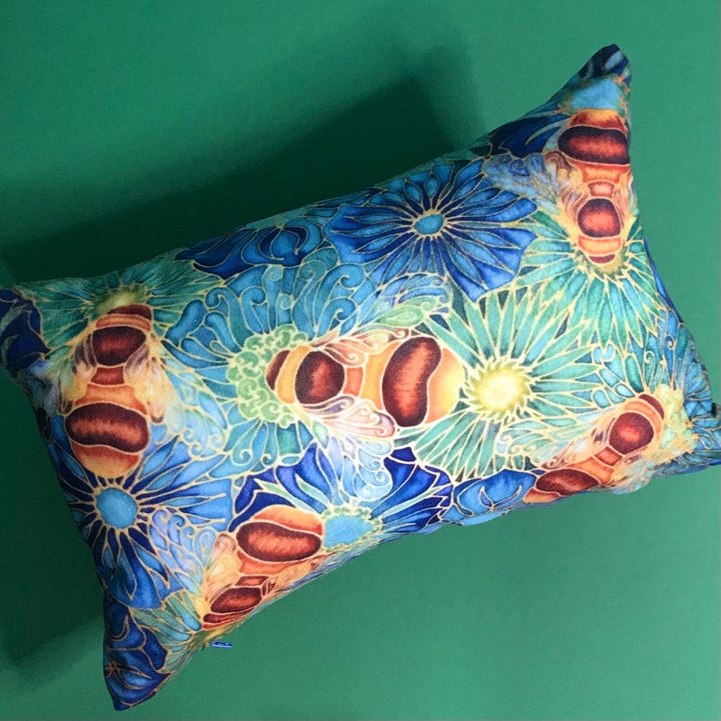 May include: A blue and yellow throw pillow with a floral pattern and bees. The pillow is made of soft fabric and has a zipper closure.