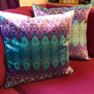 May include: Two decorative throw pillows with a teal, purple and gold geometric pattern. The pillows are on a magenta sofa.