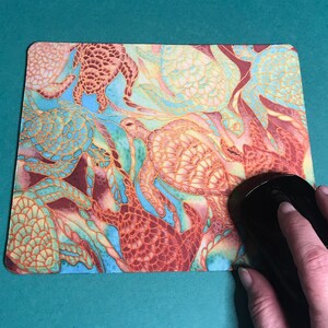 May include: A colourful mouse mat with a pattern of sea turtles in shades of orange, yellow, green, and blue.